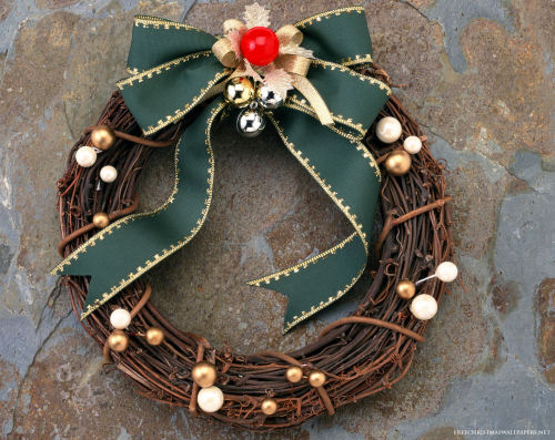 A grape vine wreath with a green bow, bells, and fold and white balls on it.