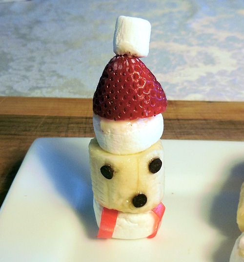 A banana marshmallow Santa head treat on top of a plate on a cutting board.