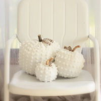 Three pumpkins on a chair made of white chenille.