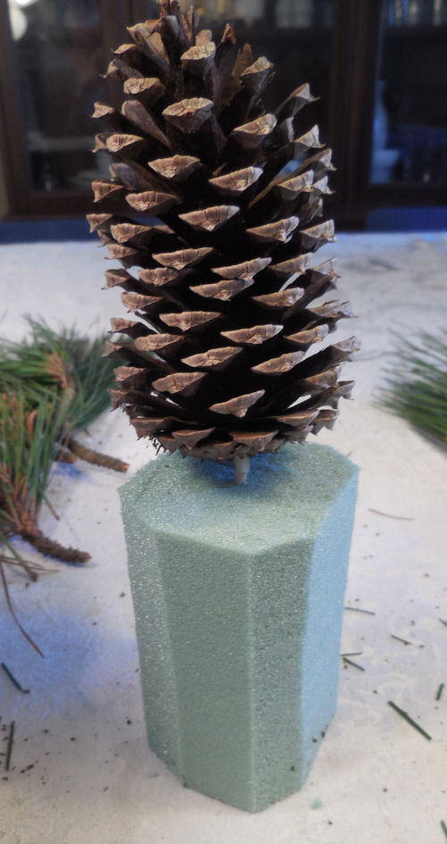 Trimmed floral foam under a pine cone.