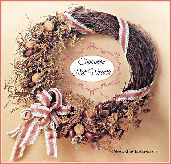 A DIY Cinnamon Nut Wreath hung on a beige wall, wrapped with a pink and white ribbon.