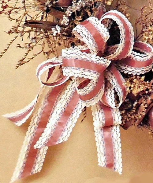 A pink and white lacy floral bow tied on a fall wreath.