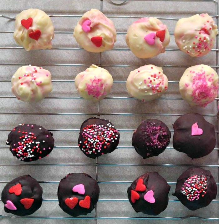 Sixteen raspberry cheesecake truffles cooling on a wire rack, the top eight have a white chocolate exterior and the bottom eight have a dark chocolate exterior.