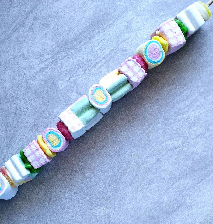 A marshmallow skewer featuring colorful assorted marshmallows on a grey slate table.