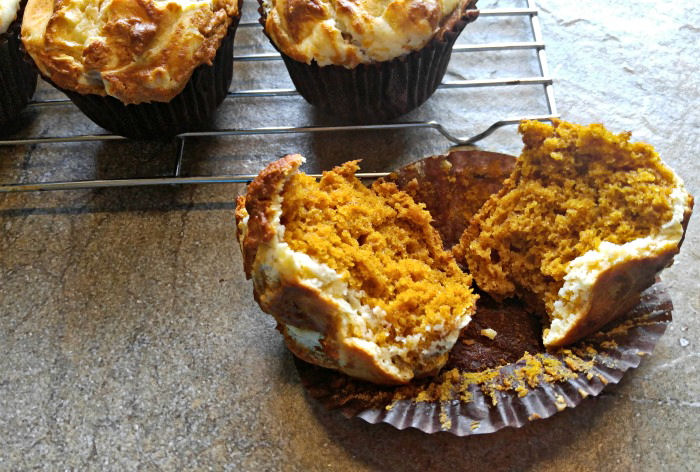 Fluffy pumpkin swirl muffins on a cooling tray, with one muffin broken open revealing an orange center.