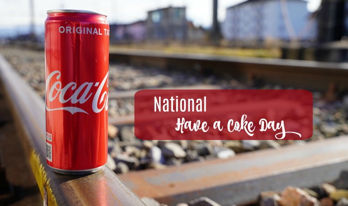 National Have A Coke Day text on a photo of a red can of Coke sitting on train tracks.