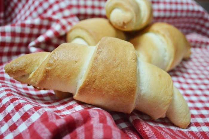 Four crescent rolls arranged on a red and white checked picnic basket liner.