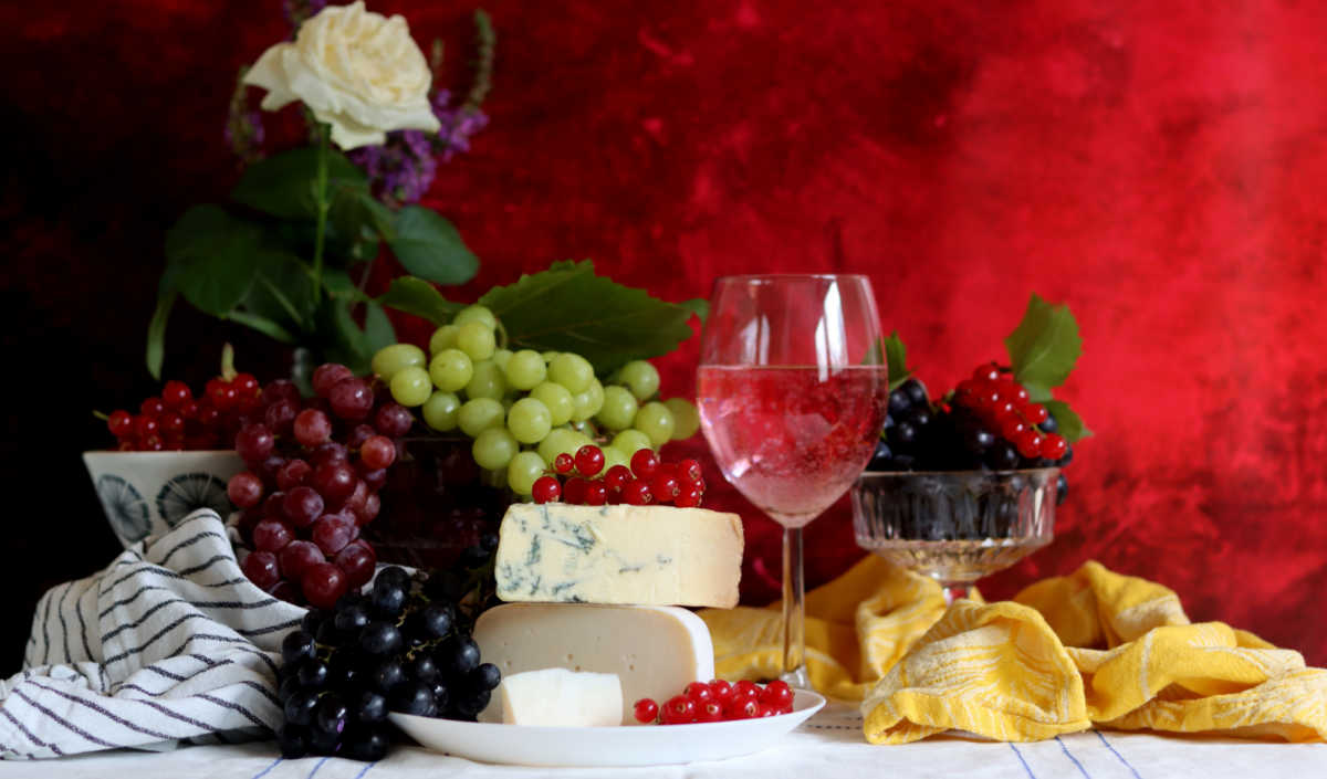 Table of food with cheese, wine, fruit and more.