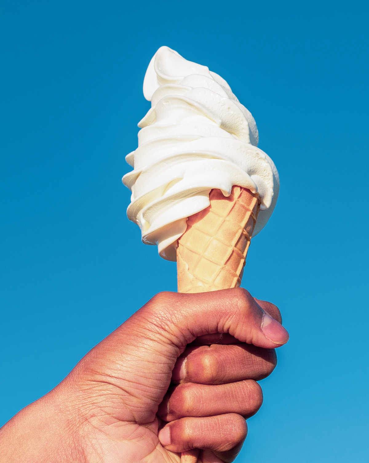 Hand holding a vanilla ice cream cone.