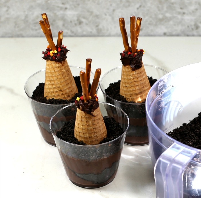 Adding Oreo crumbs to dirt cup recipe with tipis in them.