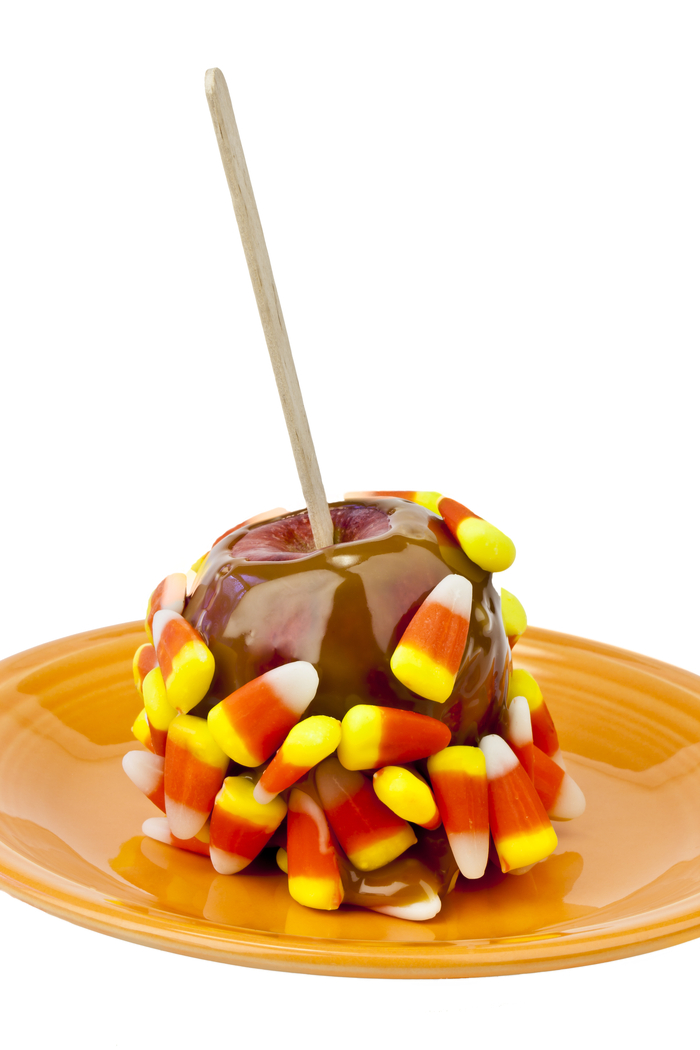 A candy corn caramel apple sitting on a plate against a white background.