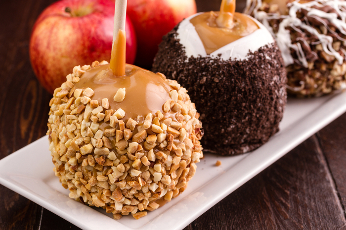 A variety of caramel apples on a plate with different toppings including peanuts, Oreos and white chocolate.
