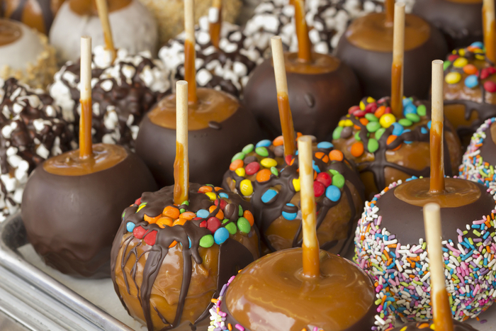 An overheard view into a display case of caramel apples with different toppings including M&Ms, sprinkles, nuts, dark chocolate, milk chocolate and white chocolate.