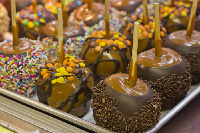 A display of assorted chocolate caramel apples with sprinkles, and other candy toppings.