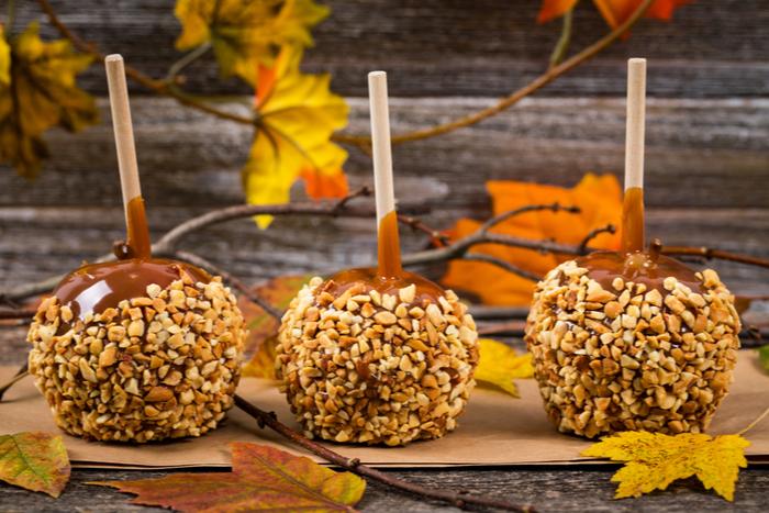 Rustic fall themed caramel apples with peanuts surrounded by fall decorations.