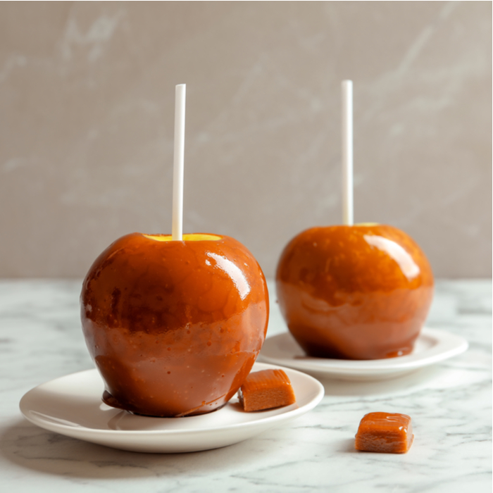 Two caramel apples on plates with caramel candy beside them.
