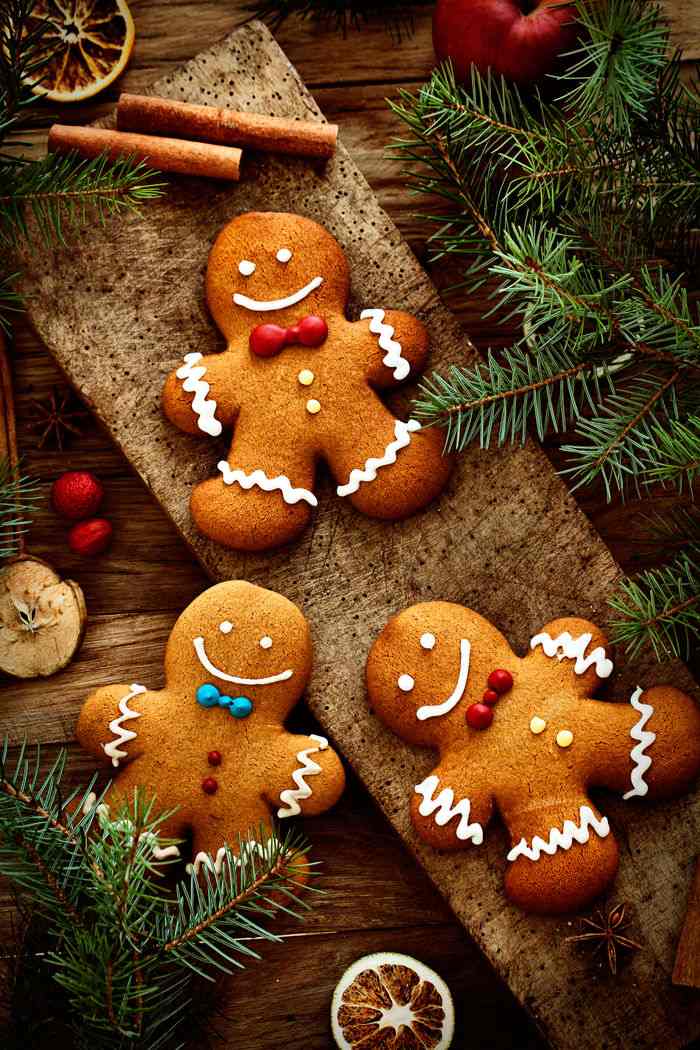 Three gingerbread cookies arranged on a table with fir branches and cinnamon sticks.