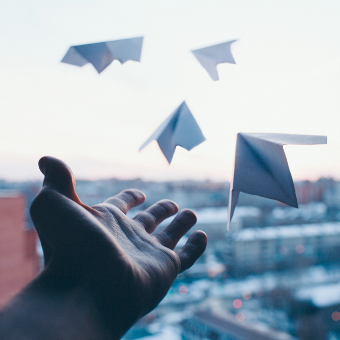 A man's hand letting go of paper planes symbolizing goals, wishes and resolutions from the window of a building in the city.