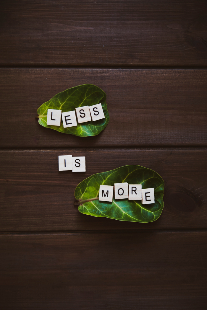 Less is more spelled out in scrabble tiles on leaves.