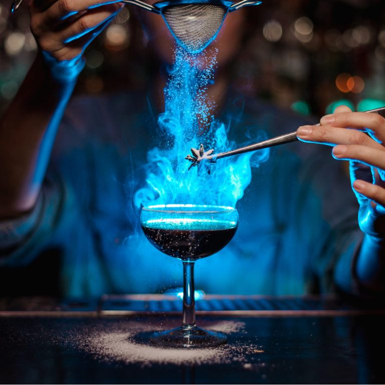 Bartender making a blue cocktail lit on fire to celebrate fun bartending facts.