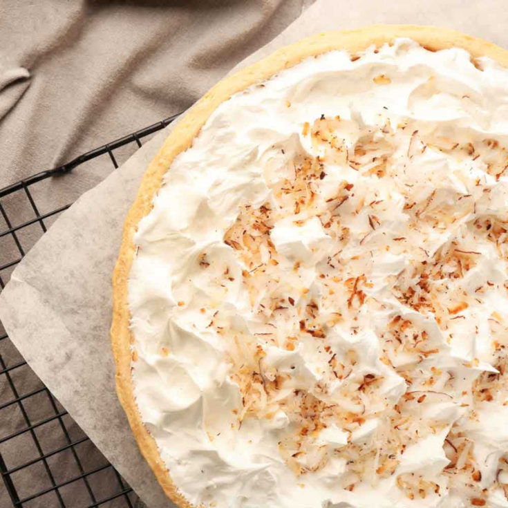 A coconut cream pie on a drying rack with parchment paper under it next to a blanket.