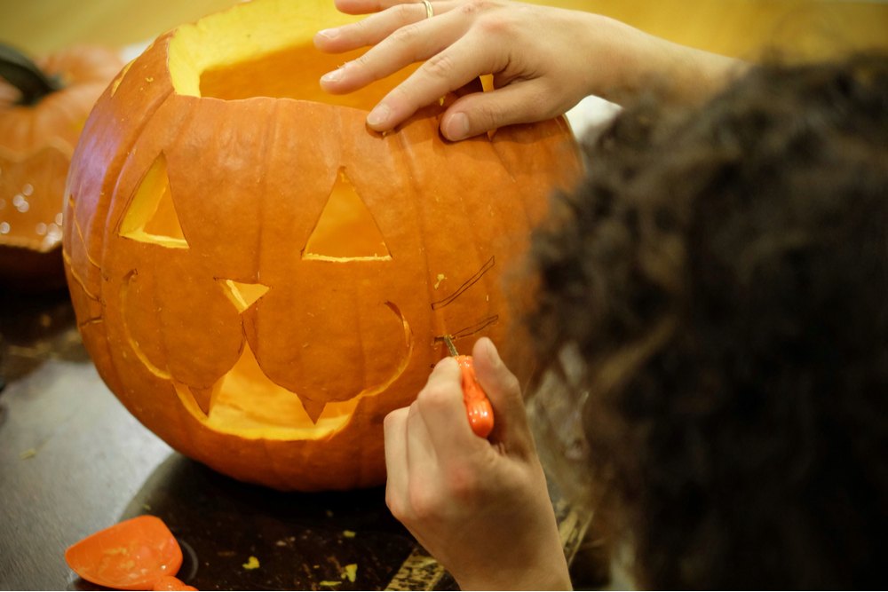 A child carving a cat jack o lantern, currently carving the whiskers.