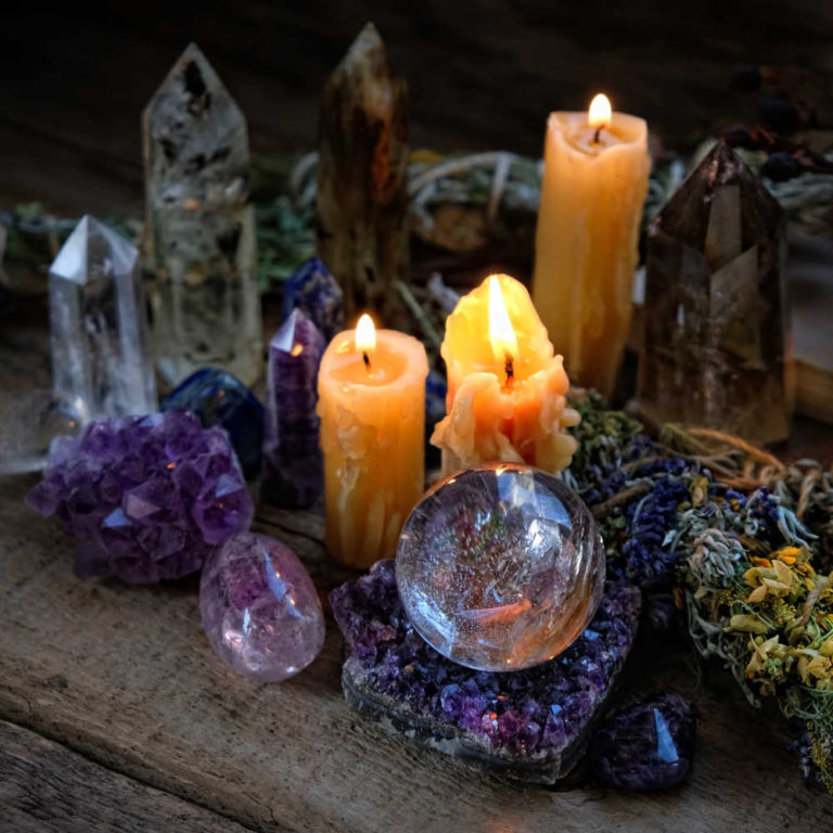 A halloween altar with candles, crystals, a sphere, and natural grassy elements that are all part of a Halloween ritual.