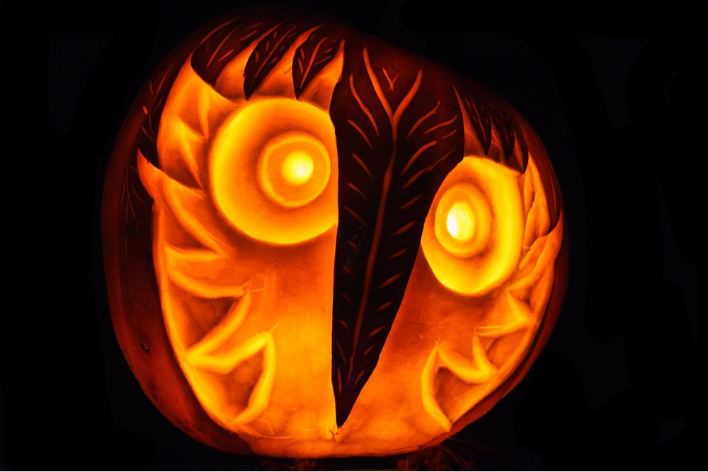 An owl pumpkin carving lit up in darkness.