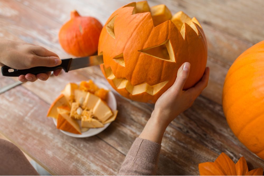 A woman's hands carving a jack o lantern on a table with a knife.