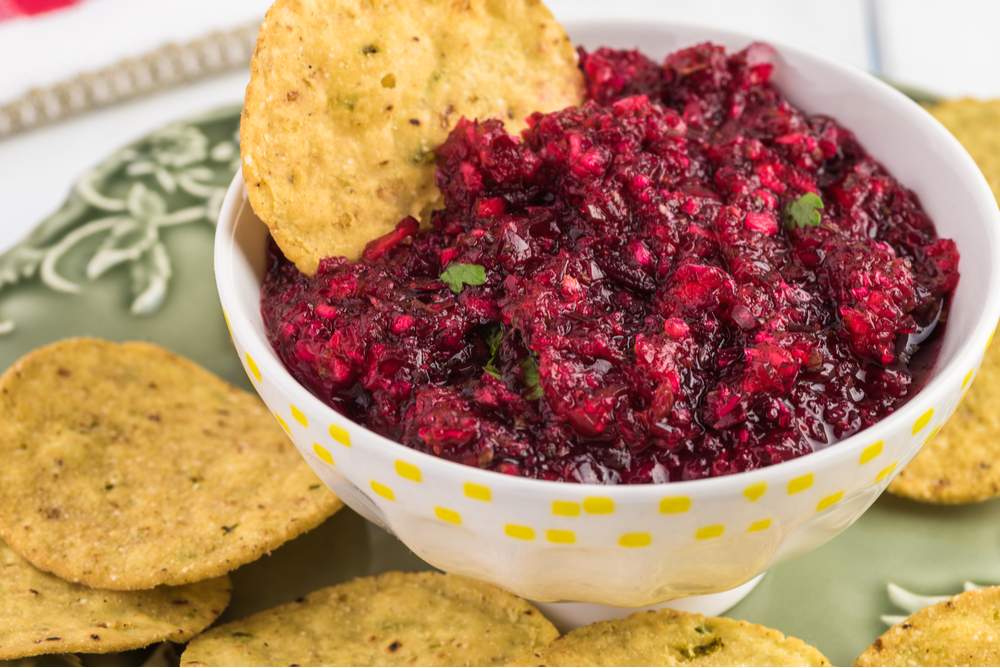 A bowl of fresh cranberry relish with chips around it on a green plate to illustrate what is cranberry relish.