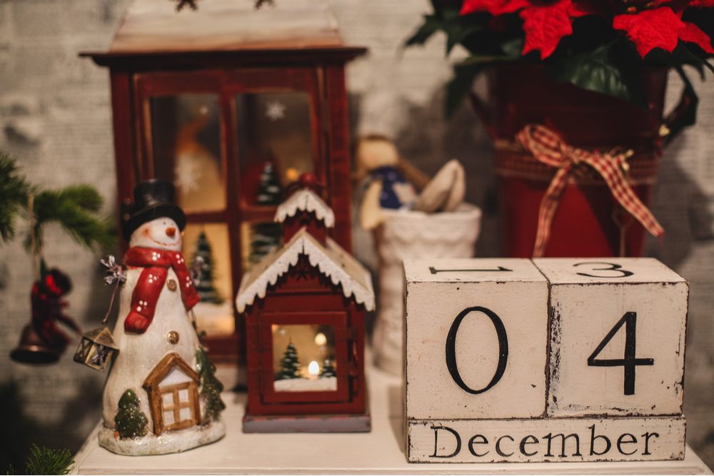 Wooden blocks that read "December 4" on a table next to various Christmas trinket decorations and a poinsettia plant in a jug.