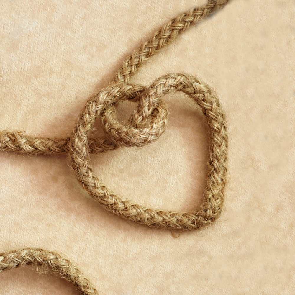 Rope formed in the shape of a heart, symbolizing a love knot on a beige background.