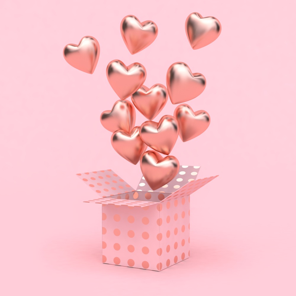 A pink box with pink heart shaped balloons coming out of it against a pink background.