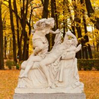 A statue of the Cupid and Psyche story during the fall, with trees dropping yellow leaves around it.