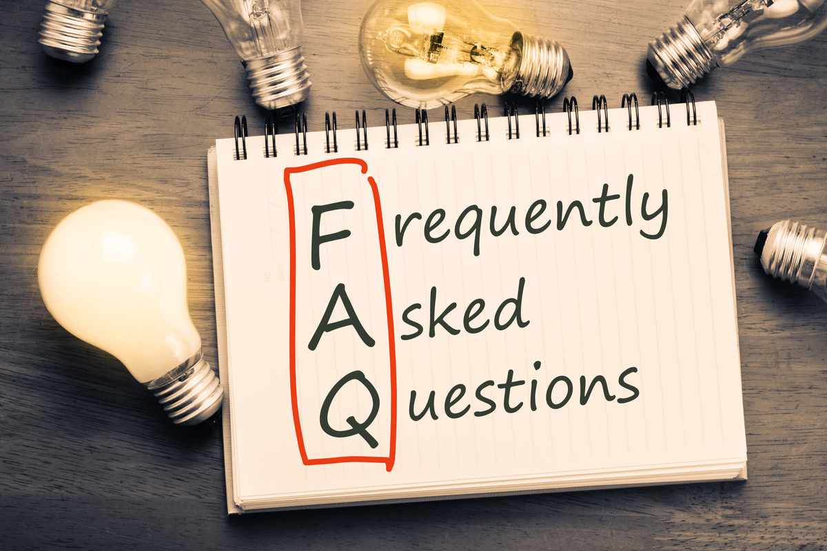 A spiral bound notebook with the words "frequently asked questions" on it, with the FAQ part circled, and lightbulbs on the table around it.