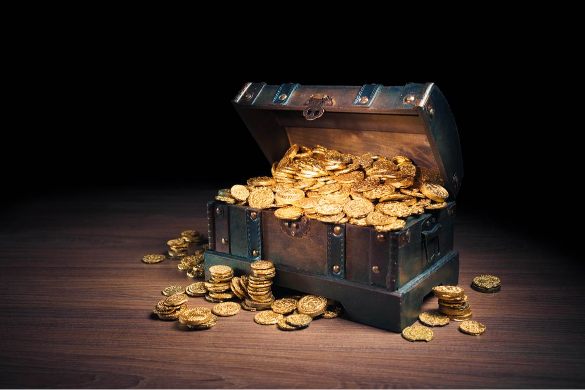 A wooden chest of gold coins on a wooden surface with a dark background.
