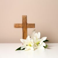 A cross against a beige background with Easter lilies beside it, to show the religious meaning of the Easter lily.