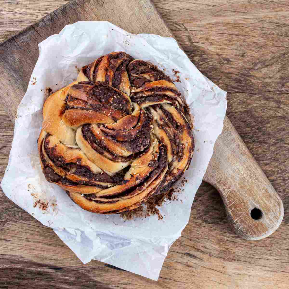 A handmade chocolate babka (Polish Easter bread) on parchment paper on top of a wooden cutting board.
