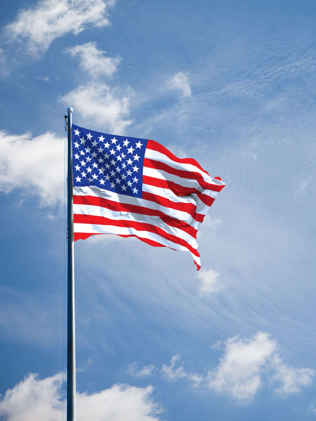 A United States flag blowing in the wind against a blue cloudy sky.