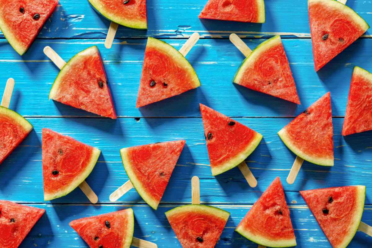 Watermelon slices with popsicle sticks in them on a teal wooden backdrop.