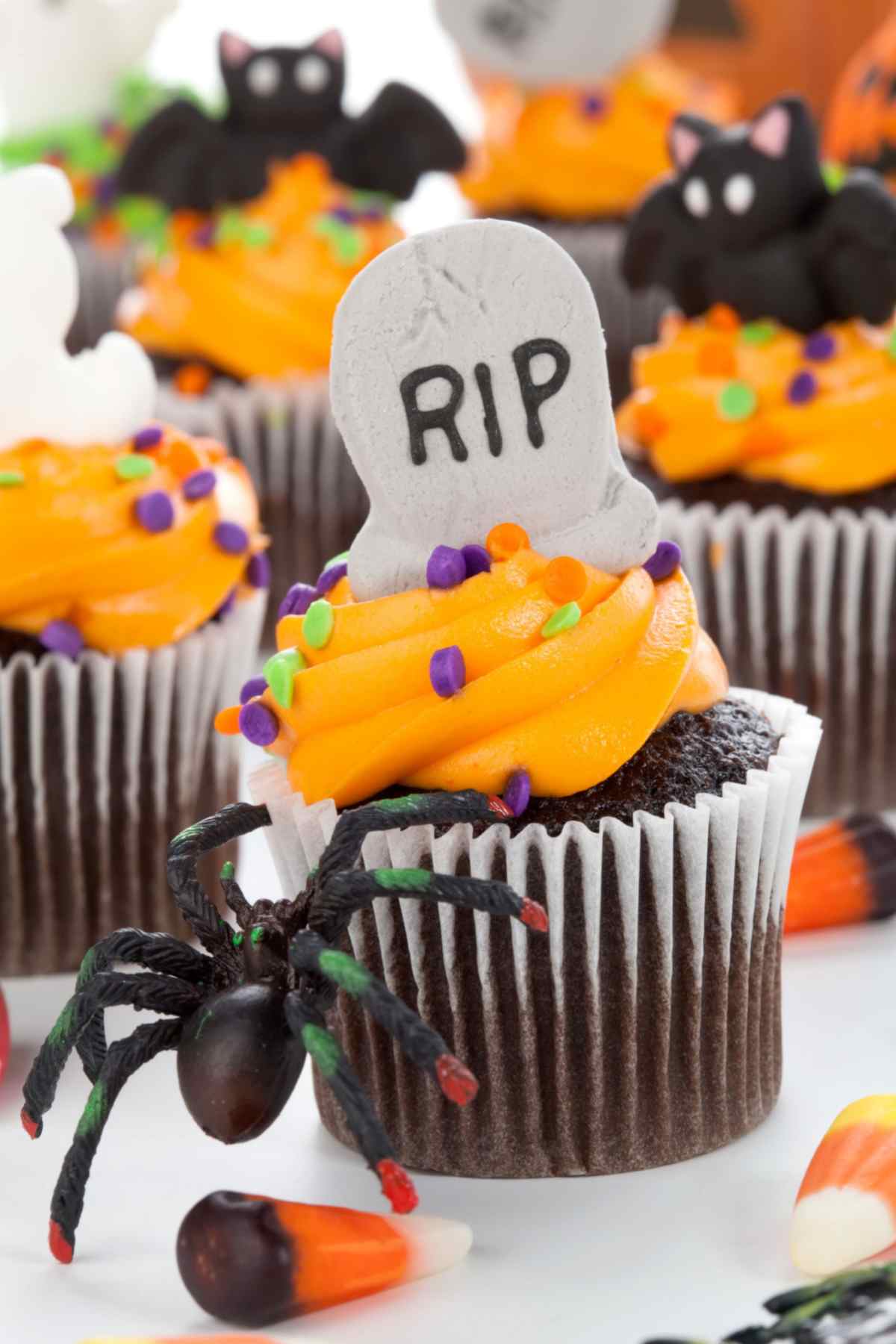 Chocolate halloween cupcakes with orange frosting and sprinkles, topped with edible bats and gravestones.