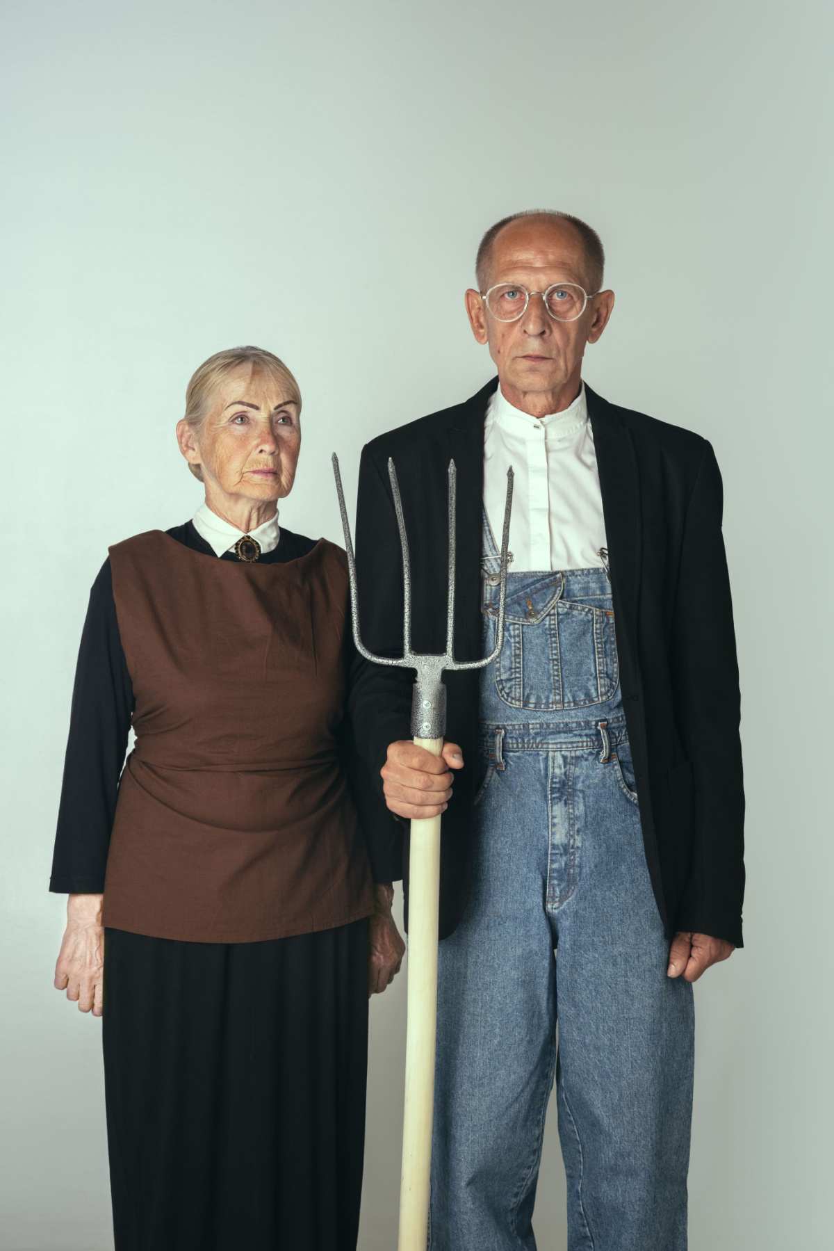 An American Gothic costume idea, where the woman is wearing a black dress, with brown vest, and the man is wearing overalls, a white shirt, and suit jacket, and he's holding a pitch fork.