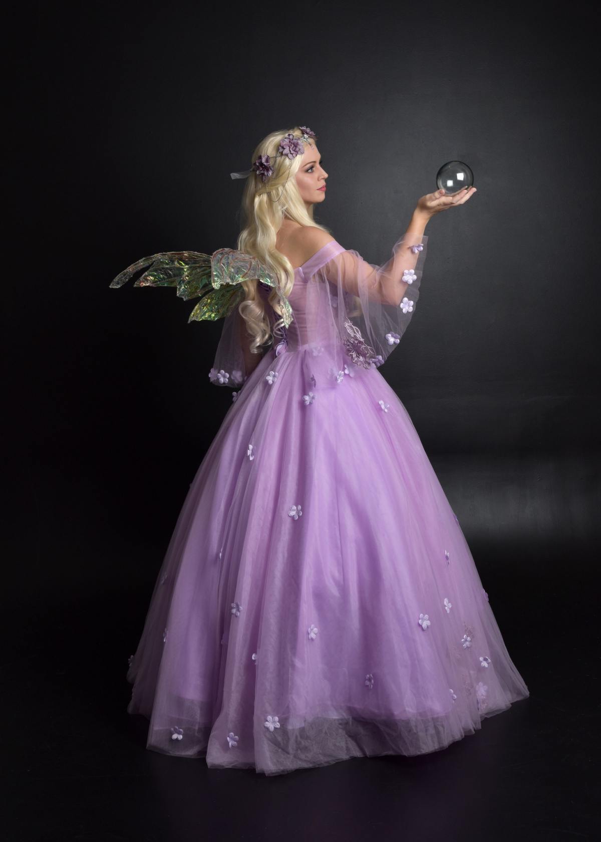 A blonde woman wearing a diy fairy costume that's a purple dress, with faerie wings, and a flower crown holding a crystal ball.