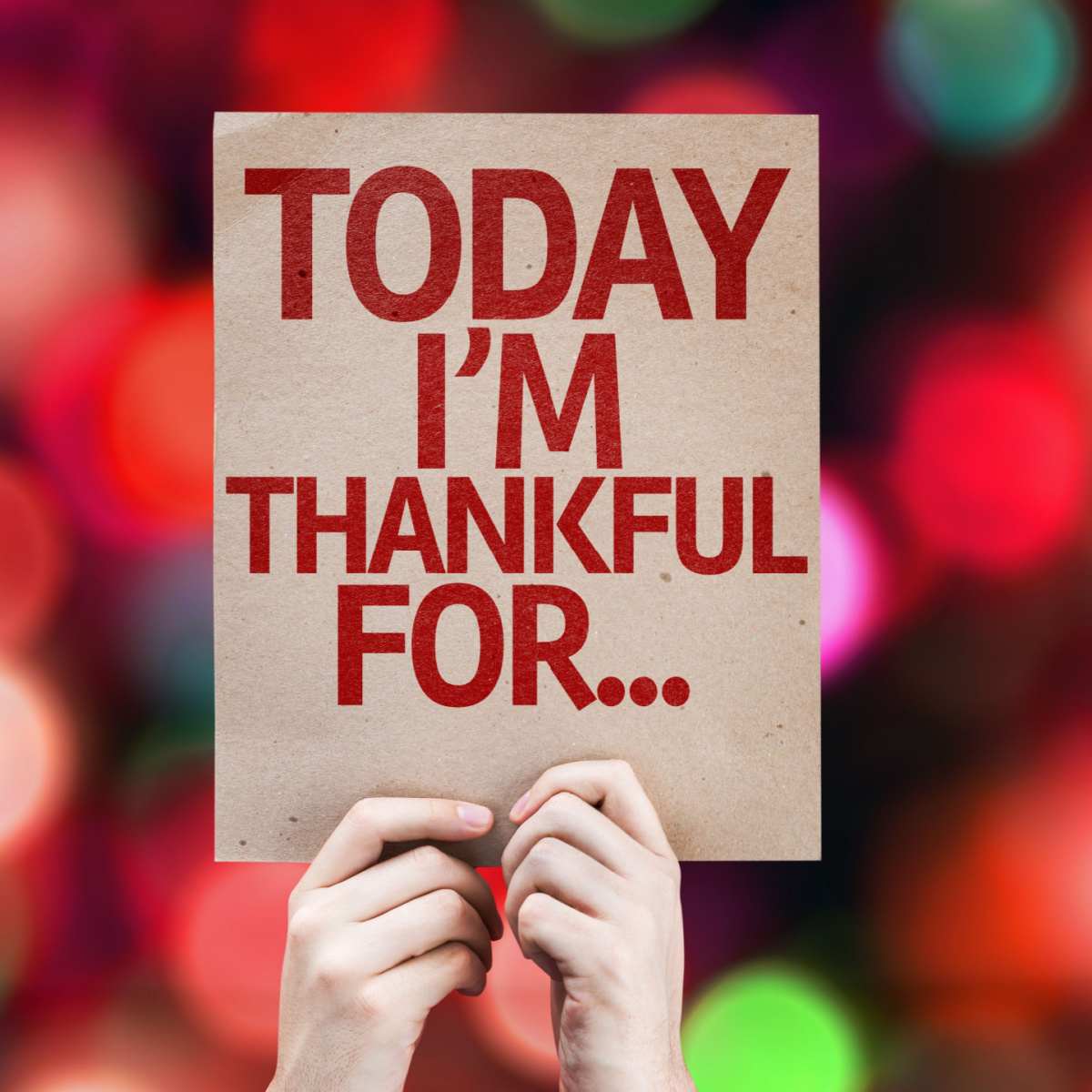 A person's hands holding up a beige sign with a gratitude journal prompt that reads "today I'm thankful for..." with a red bokeh in the background.