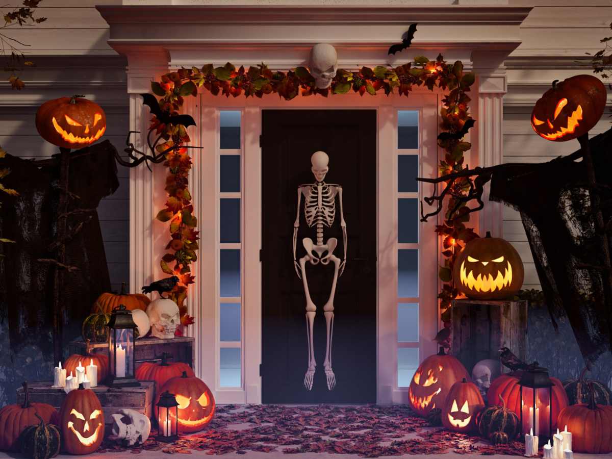 Halloween front porch decorations including a skeleton door decoration, jack o lantern scare crows, pumpkin carvings and leaf garland.