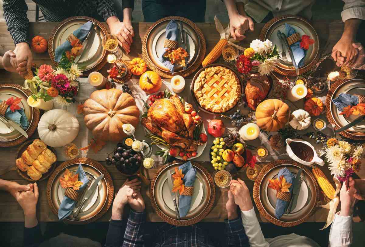 A Thanksgiving dinner table filled with food and surrounded by people getting ready to serve themselves.