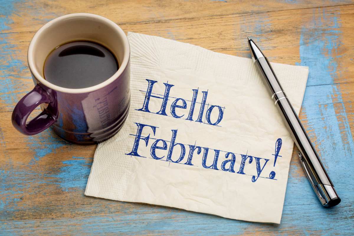 A piece of paper that reads "Hello February" with a coffee on top of it, and a pen to the right of it.