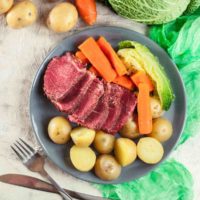 A plate of corned beef and cabbage and potatoes with vegetables, silverware and a green cloth around it to celebrate this St. Patrick's Day dinner.