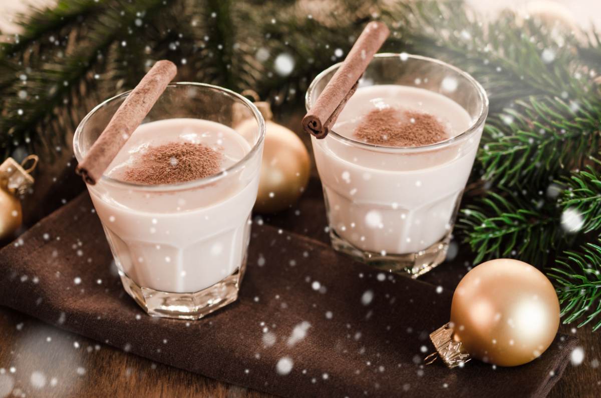 Two glasses of eggnog surrounded by pine boughs with a cinnamon stick on top of each one.