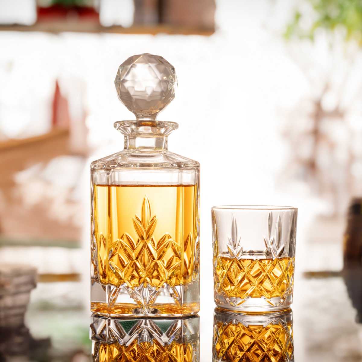 A glass decanter of gold rum sitting on a table next to a rocks glass with a pour of rum in it.